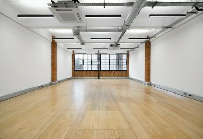 Spacious empty office room with white walls and exposed ceiling pipes.