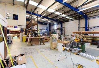 Spacious workshop interior featuring wood-cutting machinery and steel roof trusses.