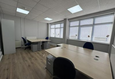 Spacious office room featuring multiple workstations and large windows for natural light.