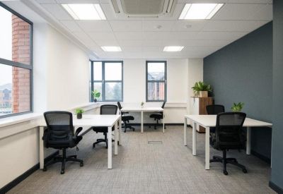 Spacious office layout with large windows, white workstations, and grey carpeting.