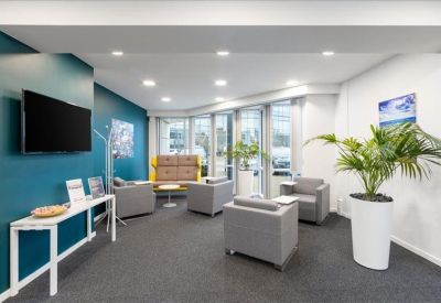 Communal lounge area with teal walls, grey armchairs, and a large wall-mounted TV.
