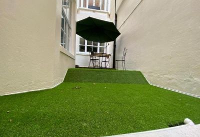 Small outdoor terrace area with artificial grass and patio furniture under a green umbrella.