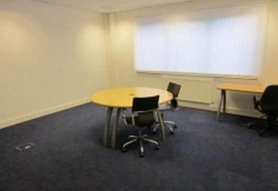 Spacious meeting room featuring a round wooden table and dark office chairs.