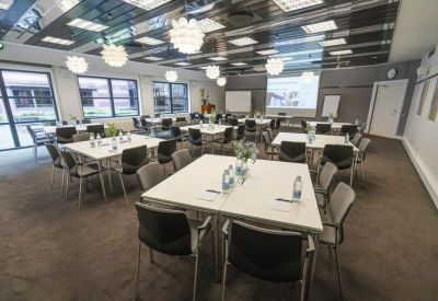 Large meeting room with square tables, black chairs, and modern pendant lighting.