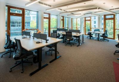 Bright open-plan office space featuring several modern white desks and ergonomic black chairs.