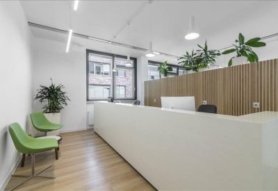 Bright reception area with a long white desk and green guest chairs.