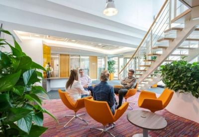 Lounge area with orange chairs, a wooden staircase, and indoor plants.