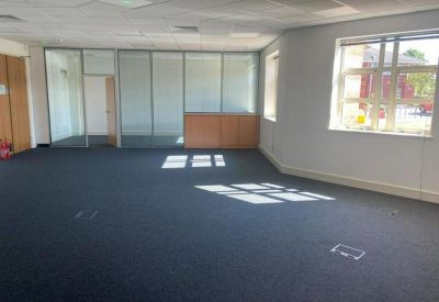 Empty open-plan office space with dark carpeting and glass partitions.