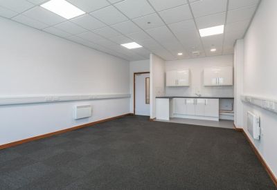 Bright empty office room with a modern kitchenette and grey carpet tiles.