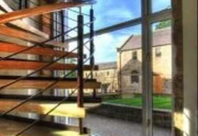 Modern wooden spiral staircase with black metal railings in a room with large glass windows.