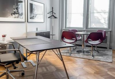 Bright private office with a dark desk, red chairs, and large windows.