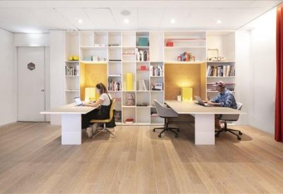 Modern workspace with a large white shelving unit separating two desks and soft wooden floors.
