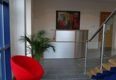 Bright reception area with a curved silver desk, vibrant red armchair, and indoor plant.