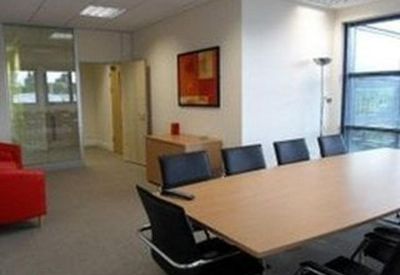 Professional meeting room with a large wooden table, black leather chairs, and a red sofa.