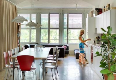 Communal dining and kitchen area with long white tables and bright red chairs.