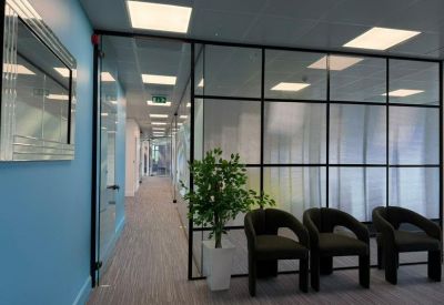 Reception or waiting area featuring a blue wall, glass partitioning, and black tub chairs.
