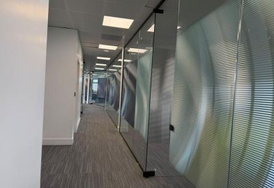 Office corridor with glass walls featuring a frosted wave pattern and gray carpet tiling.