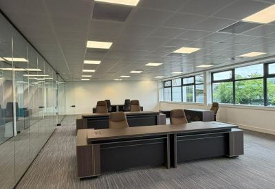 Wide-angle view of a modern open-plan office suite with dark executive desks and glass partitions.