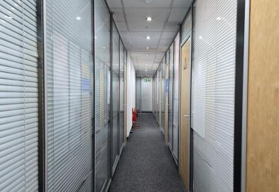 Long office corridor with glass partitions and grey carpeting.
