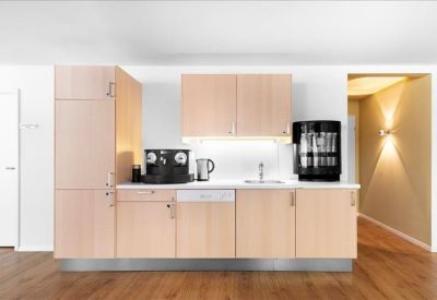Modern kitchenette with light wood cabinets, a coffee machine, and integrated dishwasher.