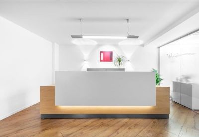 Bright white reception area featuring a minimalist desk with light wood accents and warm lighting.