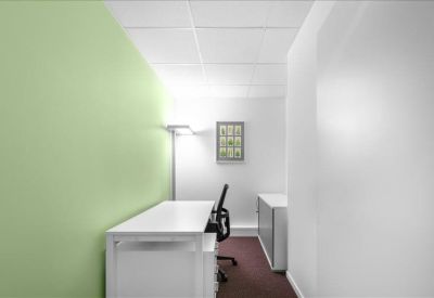 Private office featuring a green accent wall and a white desk with a black ergonomic chair.