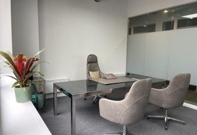 Private office suite with a modern glass desk, ergonomic chairs, and a vibrant red bromeliad plant.