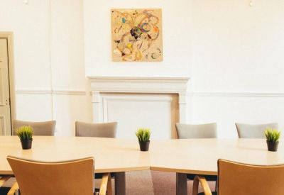 Meeting room with a light wood table, grey chairs, and abstract wall art.