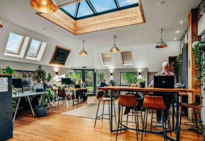 Spacious coworking space with a large skylight, wooden floors, and high-top tables.