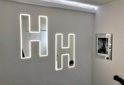Modern white wall featuring large mirrored H-shaped signage with perimeter LED lighting.