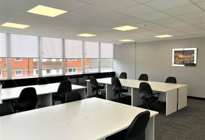 Spacious open-plan office with multiple white desks, black chairs, and large windows.