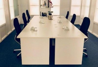 Bright boardroom featuring a long white conference table and ergonomic black chairs on blue carpet.