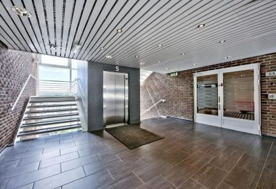 Bright office lobby featuring an elevator, brick walls, and a large staircase under a slatted ceiling.