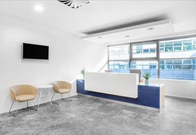 Modern reception area with a white desk, blue base, and grey flooring next to large windows.