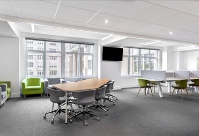Spacious breakout area featuring a central wooden table and vibrant green armchairs.