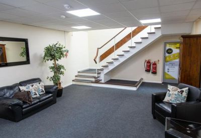 Spacious reception lobby with leather sofas, indoor plants, and a white staircase.