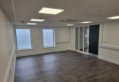 Spacious open-plan office with dark wood-style flooring and bright recessed ceiling lights.