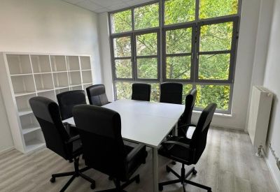 Bright conference room with a square table and views of green trees through large windows.