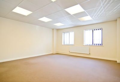 Spacious empty office with beige walls, brown carpet, and bright square ceiling lights.