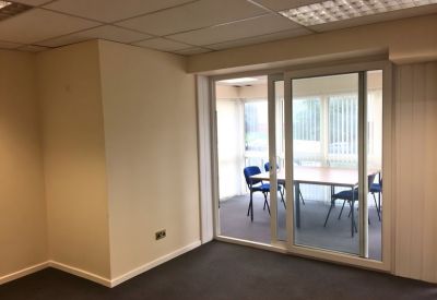 Private glass-walled meeting room with a wooden conference table and blue chairs.