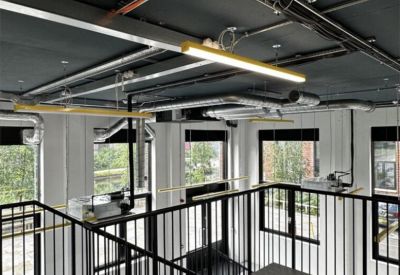 High-angle view of a workspace mezzanine with black railings and exposed ceiling ducts.