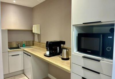Modern office kitchen with a coffee machine, microwave, and light wood countertops.