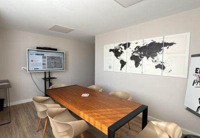 Small meeting room with a wooden table, world map wall art, and an interactive digital display.