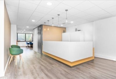 Minimalist reception area featuring a white desk with wooden accents and green chairs.