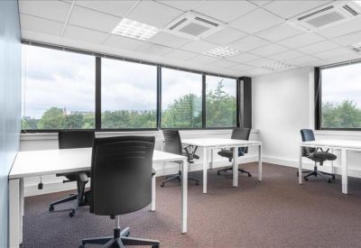 Bright open-plan office with white desks and black ergonomic chairs.