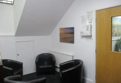 Small waiting area featuring black tub chairs and a beach photograph.
