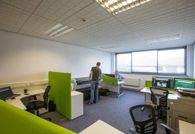 Modern open-plan office with green desk dividers and bright natural light.