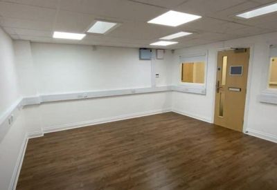 Spacious empty office room with wood-effect flooring and white walls.