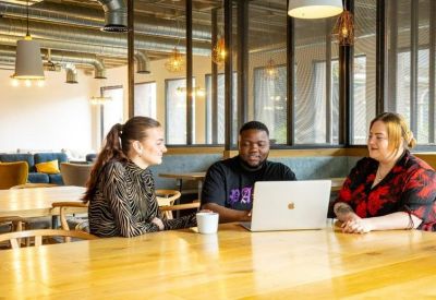 Coworking table with people working on laptops under industrial ceilings.
