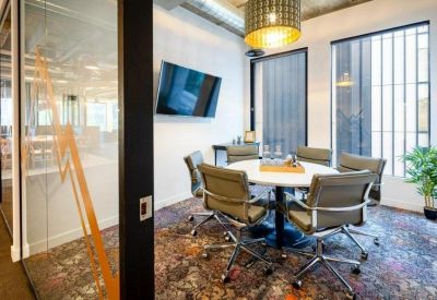 Professional meeting room with a round white table and a wall-mounted screen.
